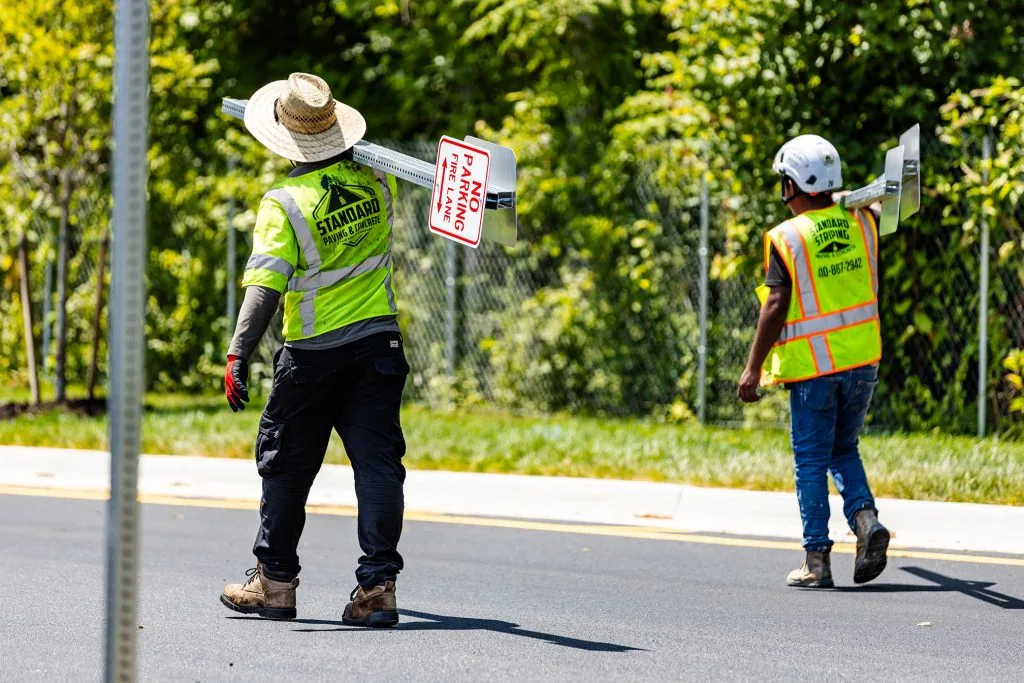 Two employees of Standard Paving & Concrete carrying parking lot signs